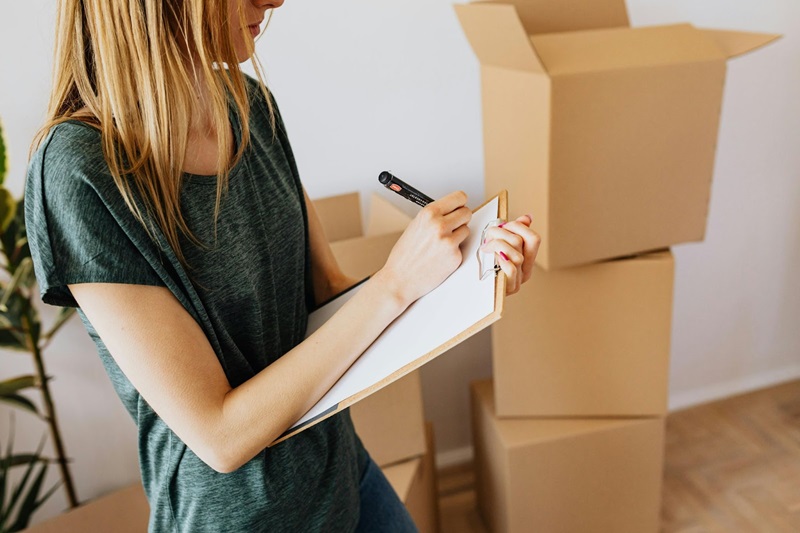 female writing on clipboard inventorying moving boxes